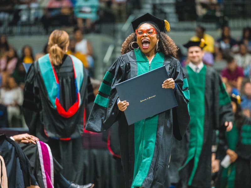 Excited School of Medicine graduate holding degree at commencement.